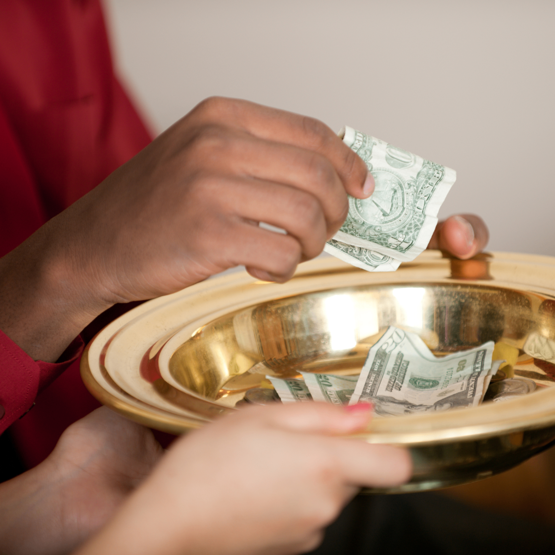Hands placing an offering into a golden collection plate